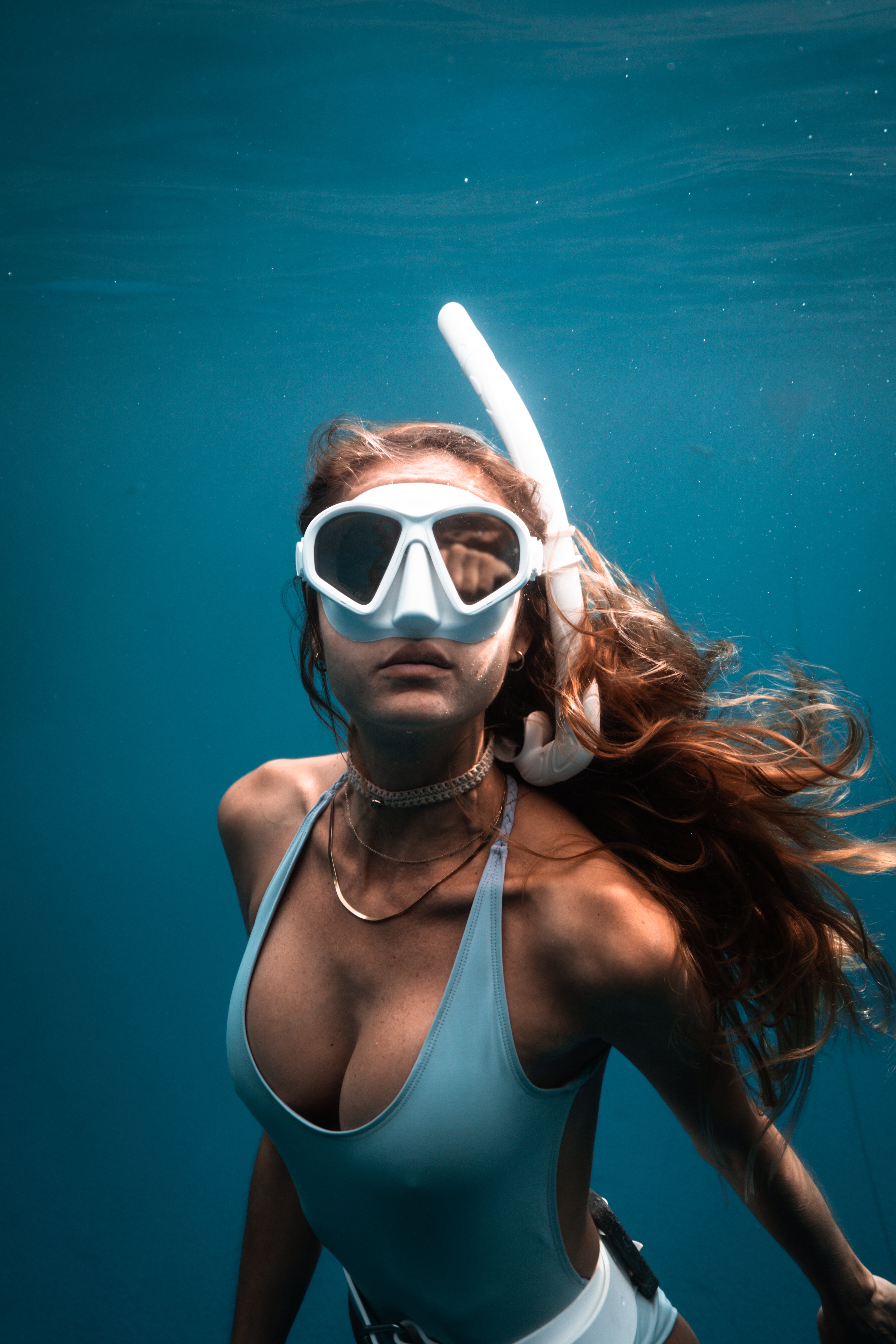 Person snorkeling underwater wearing a blue swimsuit and white snorkel mask.